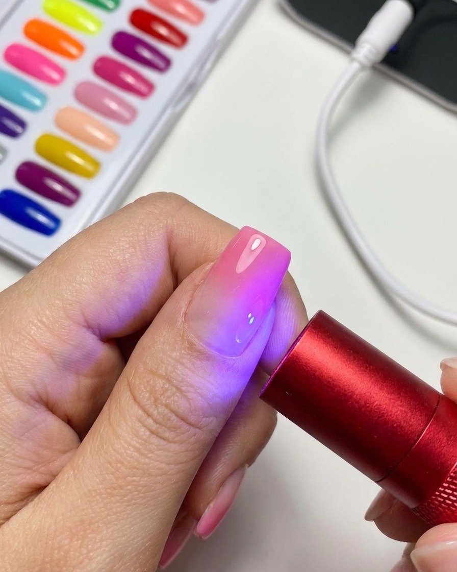 A portable red UV/LED curing lamp lighting up a finished magnetic cat-eye gel nail.