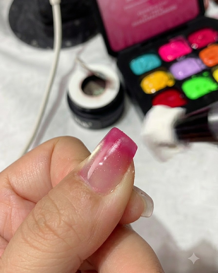 A sponge applicator dabbing magenta red gel polish onto the tip of a fingernail to build a gradient.