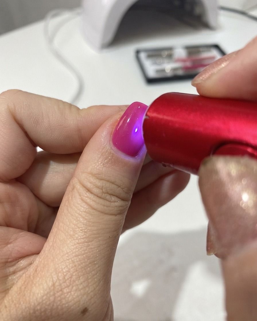 A portable red UV/LED lamp curing the gel polish on a fingernail.