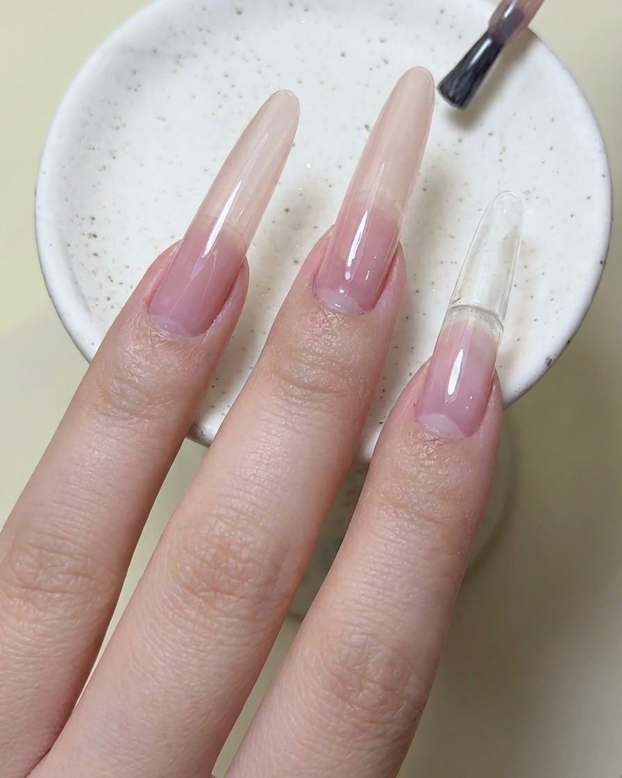 A nail brush applying magenta red gel polish onto the index fingernail.
