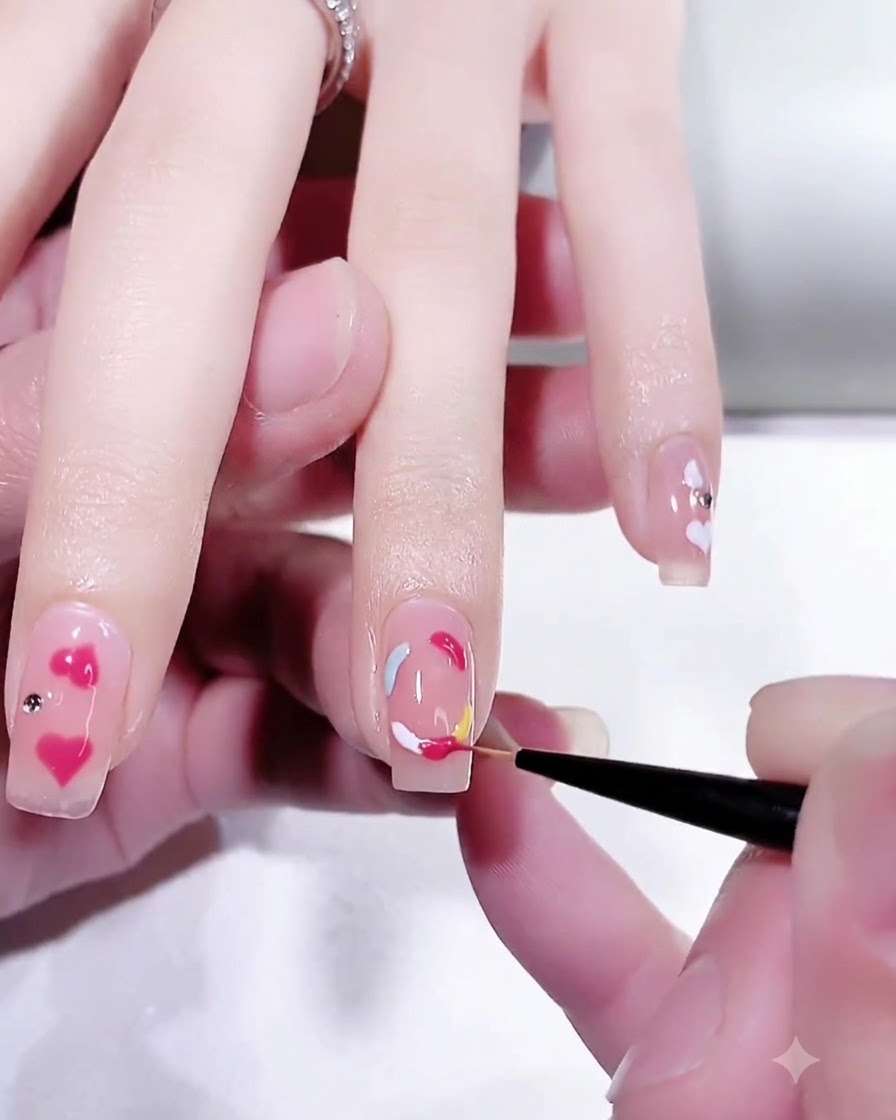 Close-up of a fine detailing brush refining the vibrant peach pink section of a multicolored gel ring design on a fingernail.