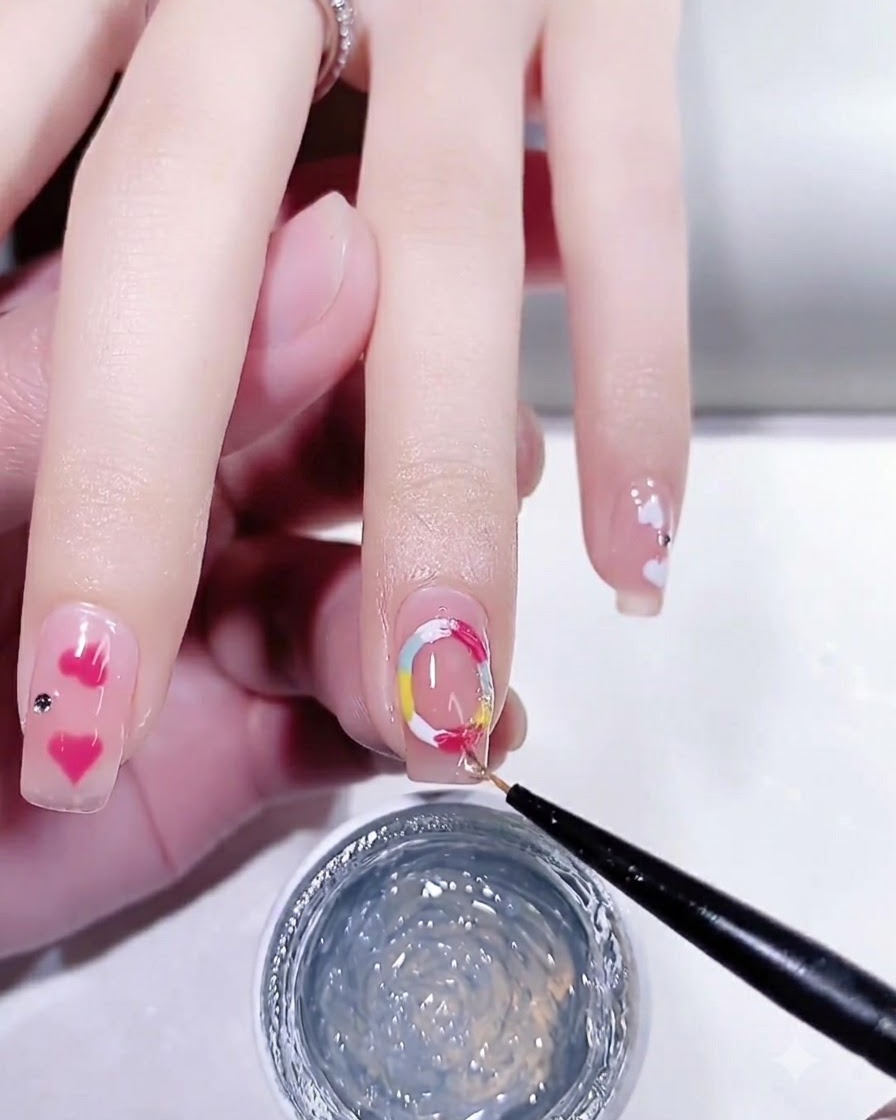 A fine nail art brush applying a glossy top coat over a manicured nail with colorful dot details.