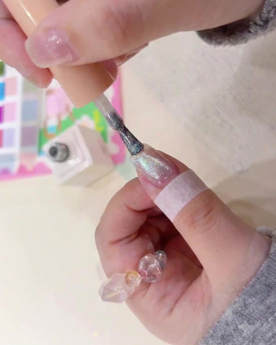 A brush applying shimmery magnetic amber gel onto a natural fingernail.