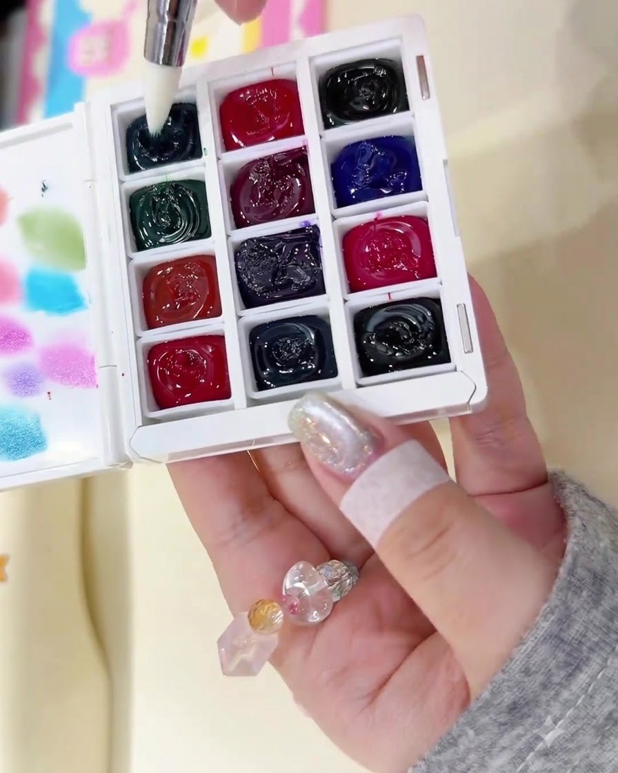 A fine brush dipping into a dark ink well on a partitioned watercolor palette.