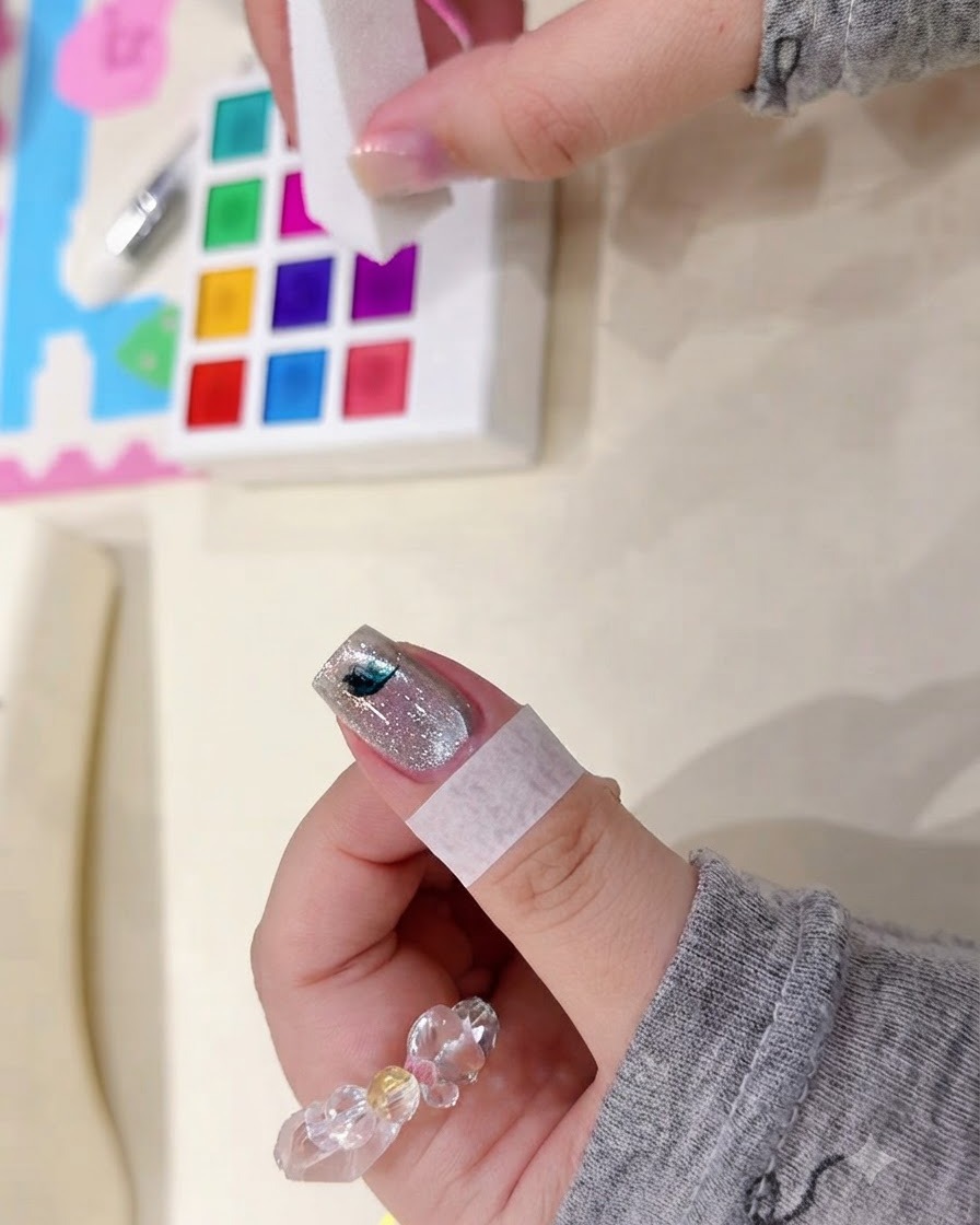 A sponge block tapping a small dark blotch of watercolor pigment on a shimmering nail surface.