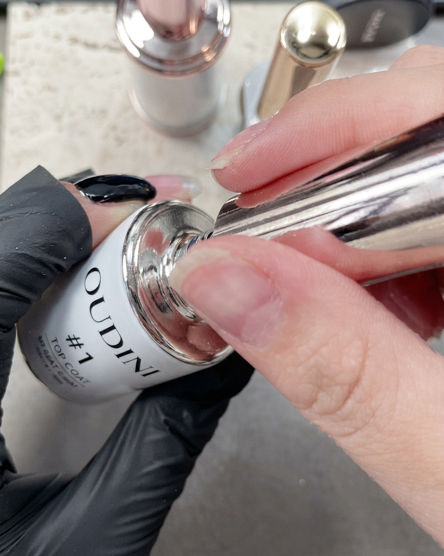 A close-up view of a fine brush applying top coat along the edge of a manicured index nail.