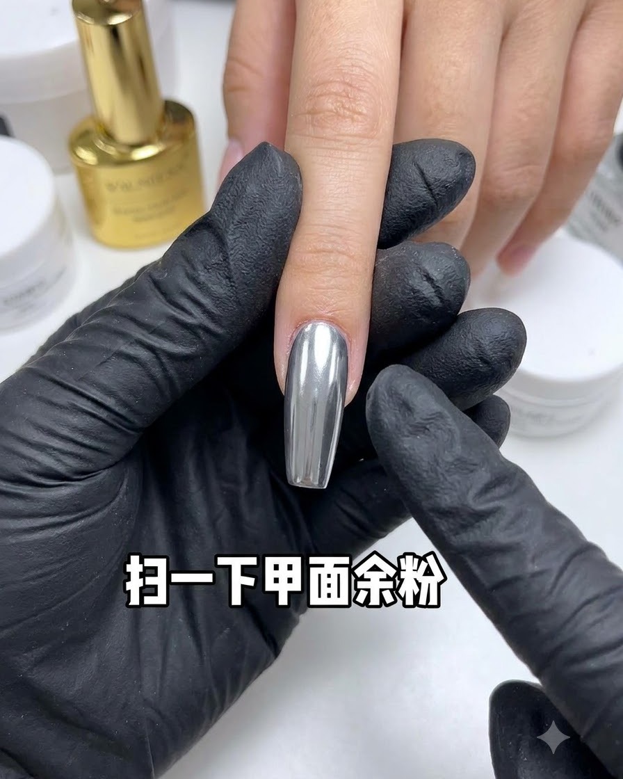 A dusting brush sweeping away excess powder from a reflective chrome nail.