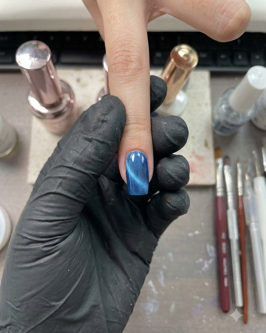 A single finger with a glossy blue cat-eye finish positioned under a nail studio setting.
