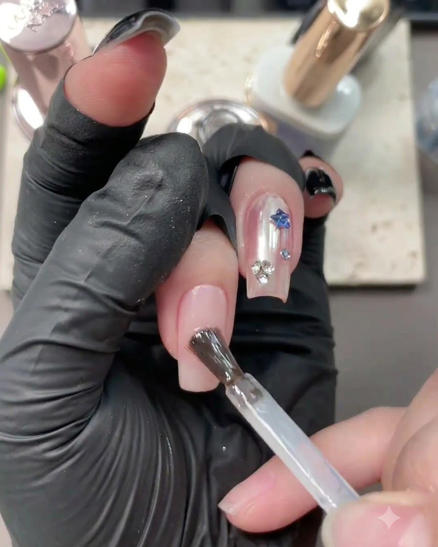 A brush applying clear base gel onto a neutral nude nail with existing nail art.