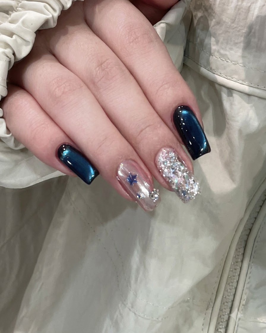 A finished hand showing deep blue cat-eye nails alongside a star-embellished accent nail and a full glitter nail.