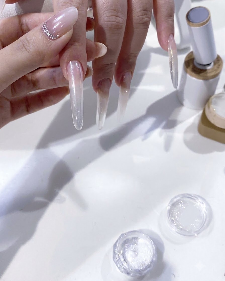 A close-up view of a brush carefully applying white gel pigment to shape a French tip on an extended nail.