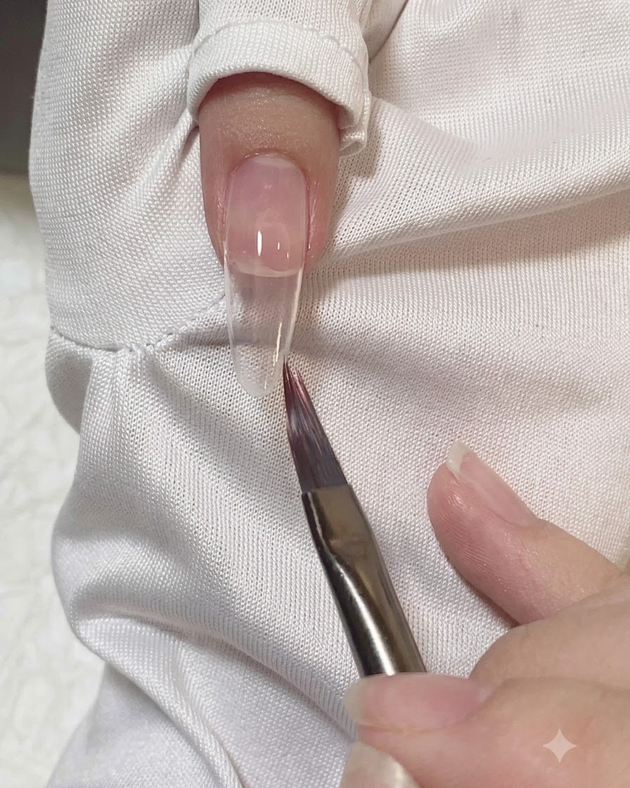 A flat brush smoothing and blending the edges of pink gel on a nail.