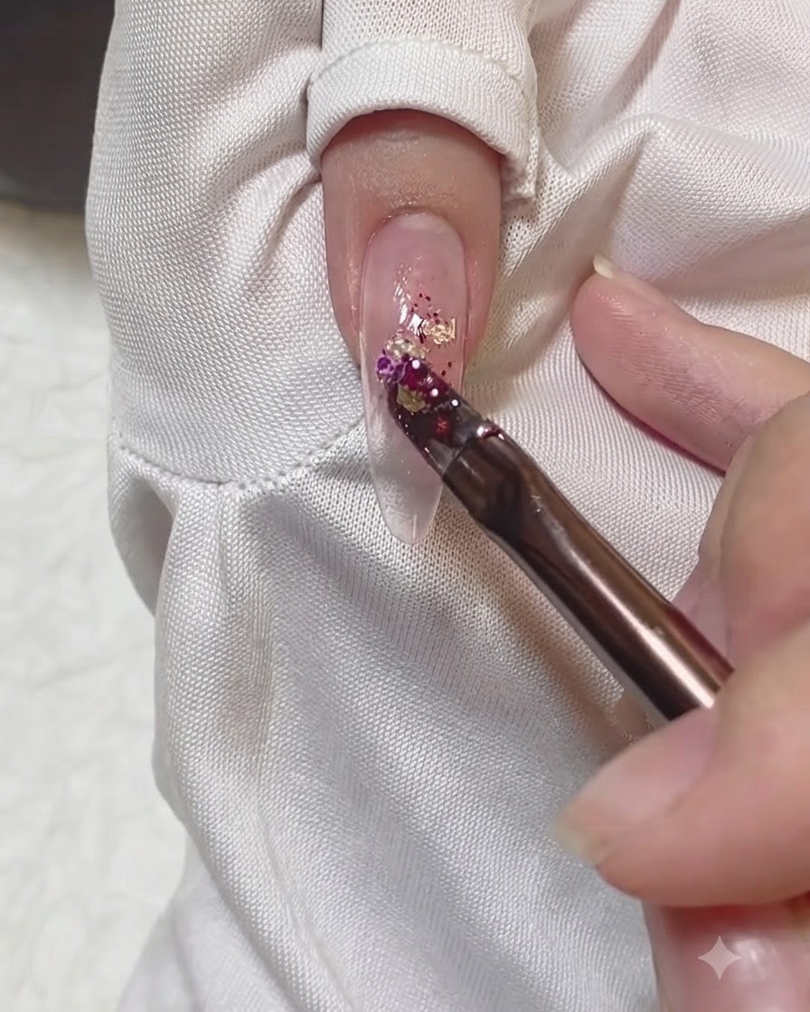 A brush applying a cluster of colorful glitter flakes down the center of a nail.