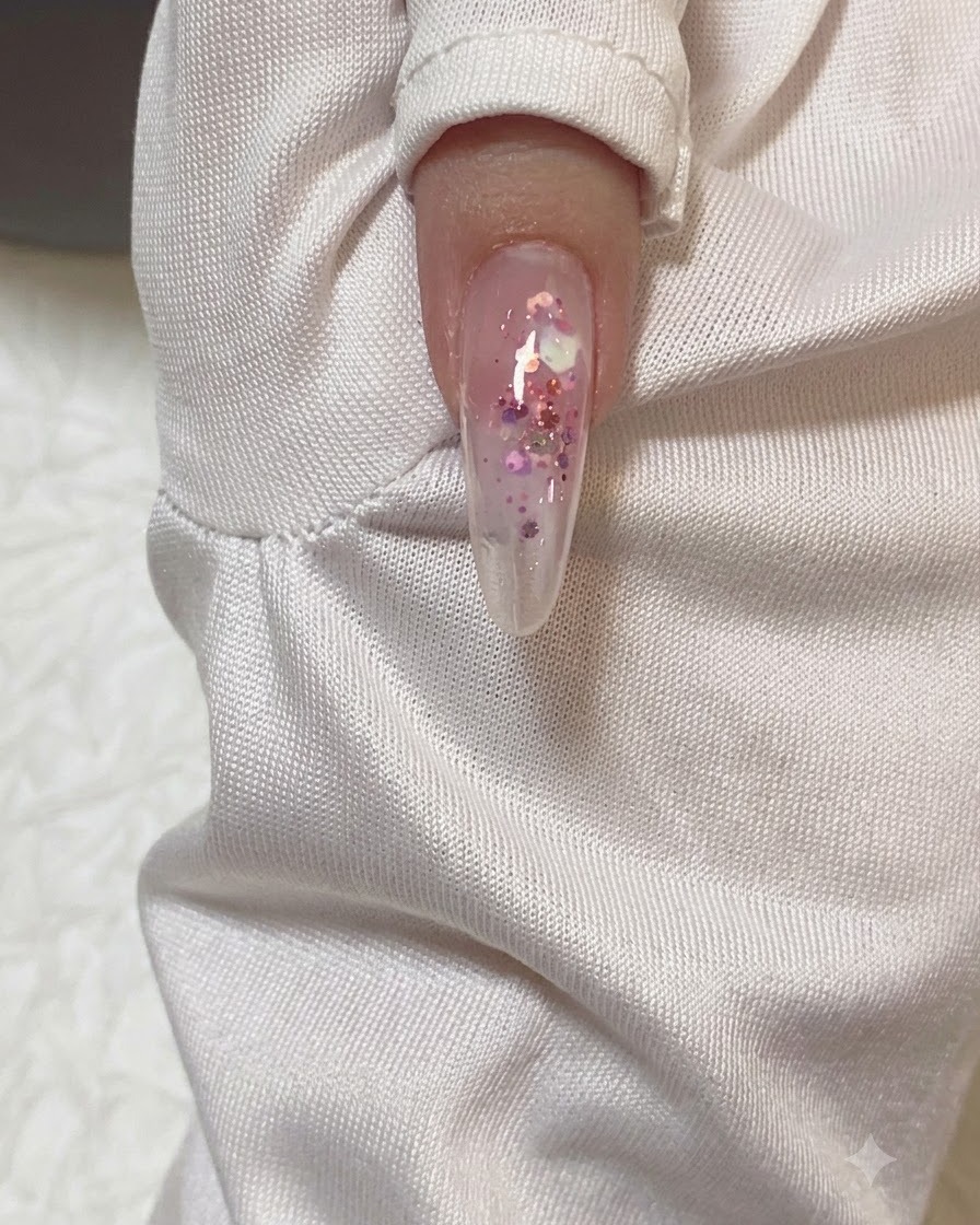 A close-up view of an almond-shaped nail receiving a clear coat of builder gel.