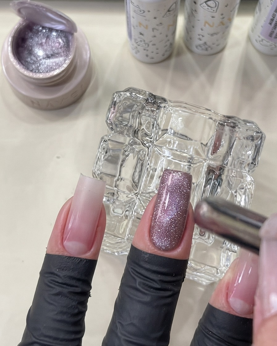 A magnetic tool held near a manicured nail to shape the flashing cat eye gel into a glowing glass bead effect.