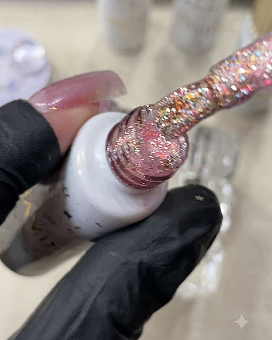 A brush holding warm orange glitter gel above a nail.