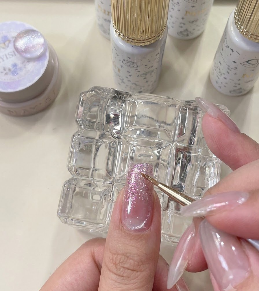 A fine liner brush blending an orange glitter accent on a manicured nail.