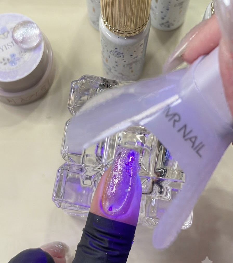 A mini UV lamp curing a decorated nail under purple light.