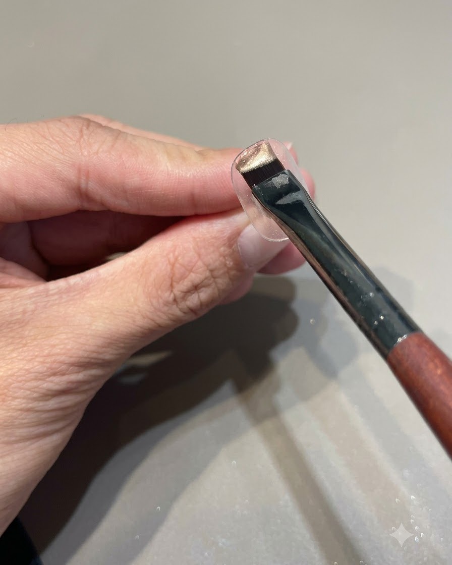 A brush loaded with pink gold cat eye gel polish held over a clear nail display stand.