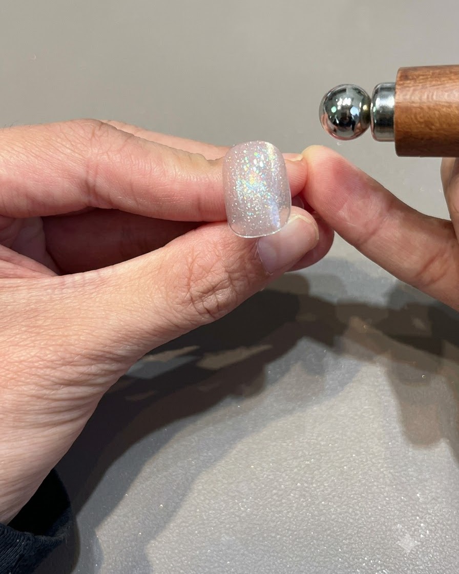 A spherical magnet held near a shimmering pink gold cat eye gel nail to shape the light band.
