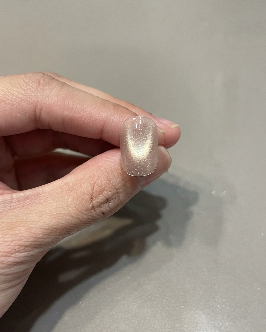A single manicured nail featuring a cured pink gold cat eye polish with a centered light reflection.