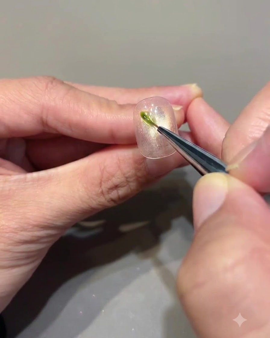 A fine liner brush applying a small vertical stroke of avocado green gel onto a cat eye nail.