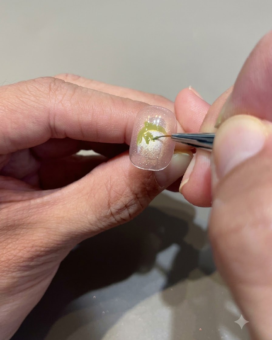 A close-up view of a fine brush meticulously filling in avocado green gel to create strawberry leaves on a nude pink nail.