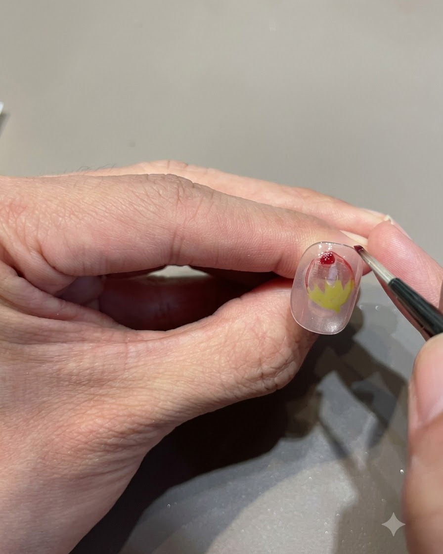 A close-up shot of a fine brush adding a drop of red glass gel to enhance the strawberry gradient.