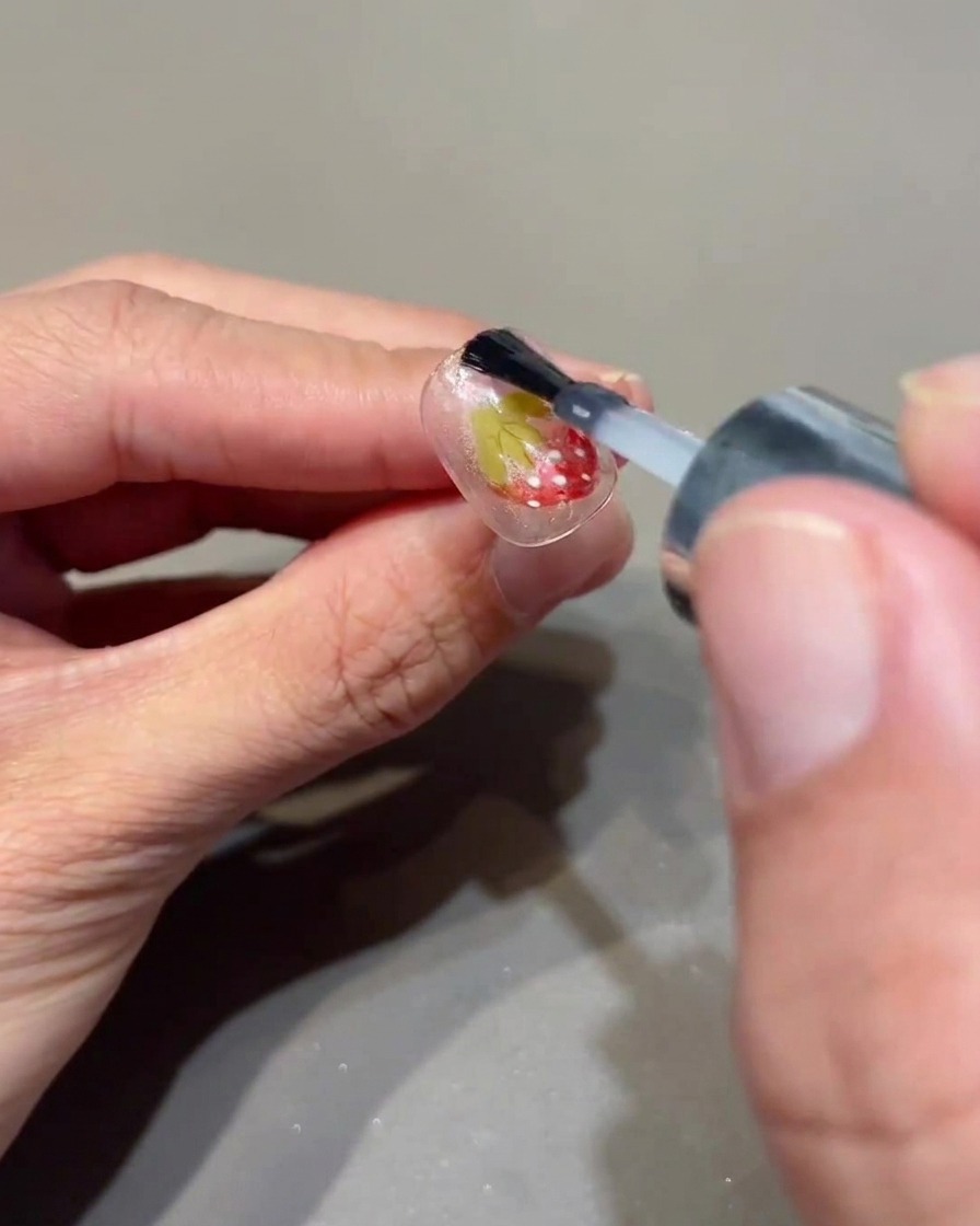 A brush applying a clear top coat over a decorated nail.