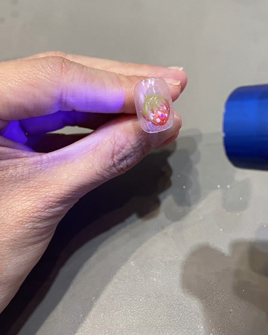 A portable UV flashlight curing a 3D strawberry nail design.