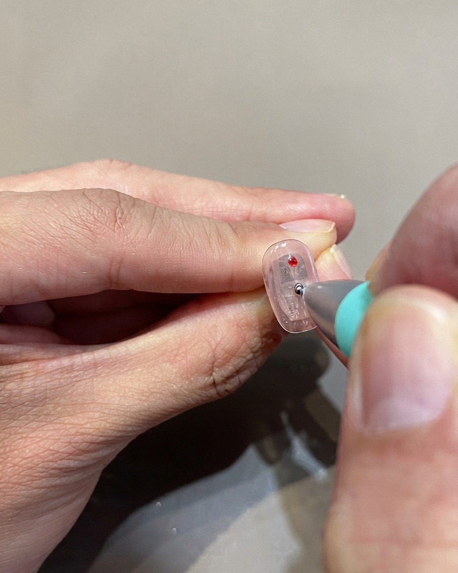 A dotting tool placing red glass gel polka dots onto a clear nail surface.