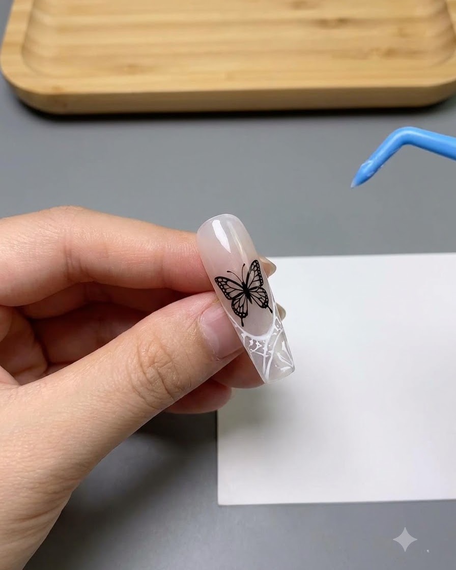 A close-up of a nail decorated with a detailed white hollow butterfly pattern.