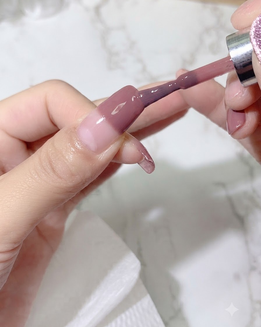 A brush applying a second coat of colored gel onto the nail to intensify the gradient shade.