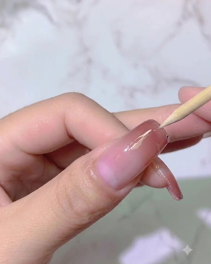 A wooden tool guiding placement or adjustment near the nail surface under lighting.