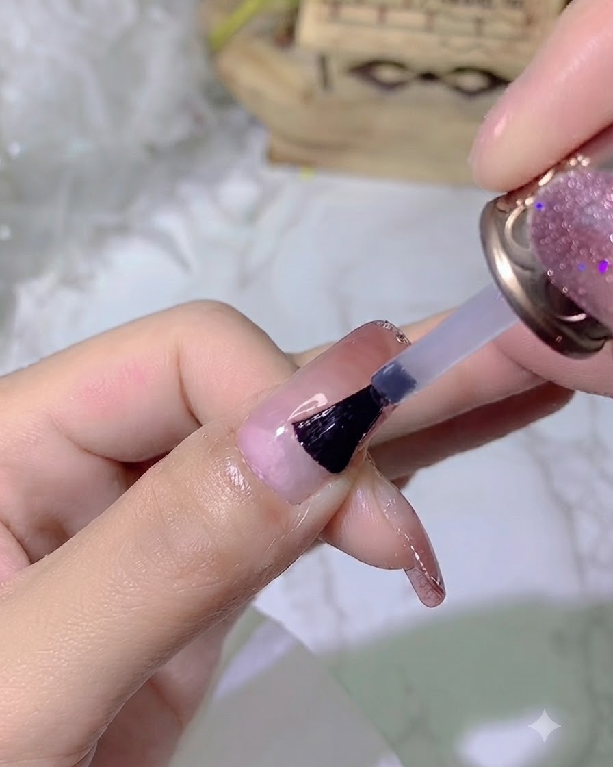 A brush applying a clear glossy top coat onto a manicured nail.