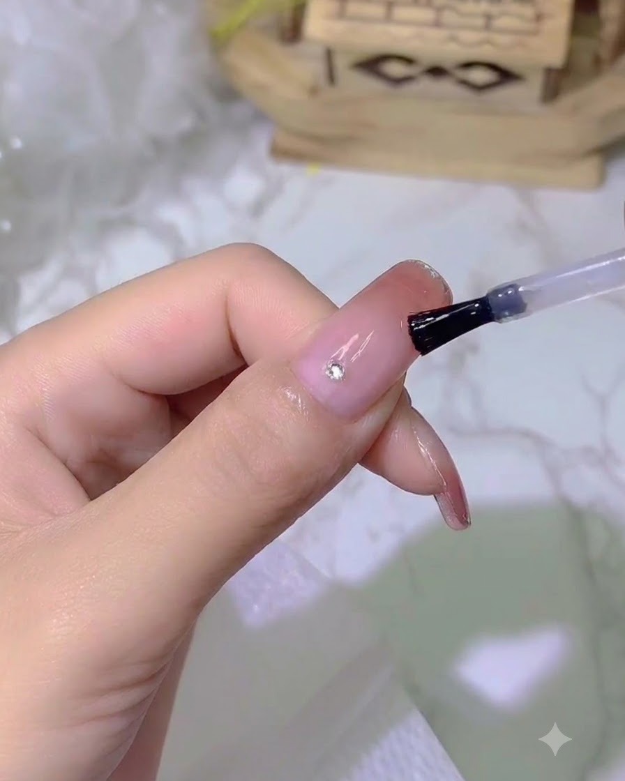 A tiny sparkling crystal being placed onto a nail using a detail tool.