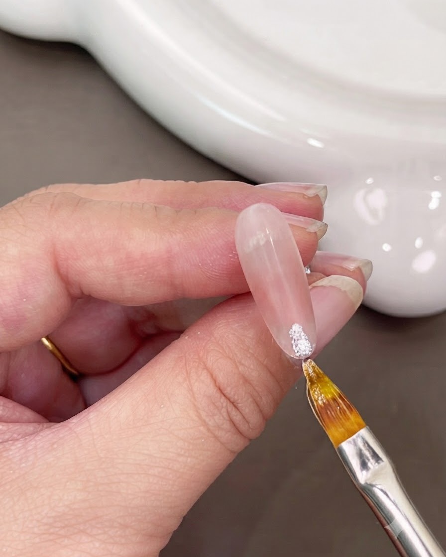 A fine brush applying sparkly white gel onto the tip of a nail.