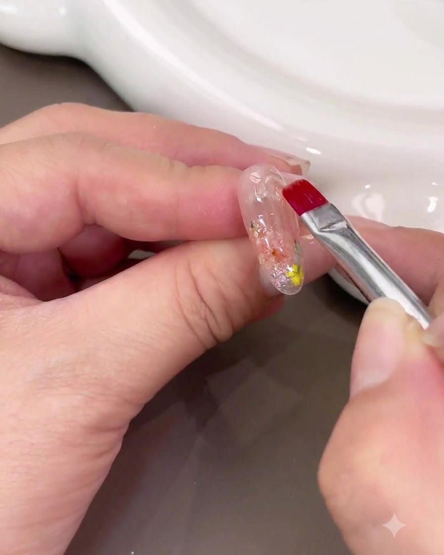 A nail brush applying a thick layer of clear builder gel over the dried flower nail art.