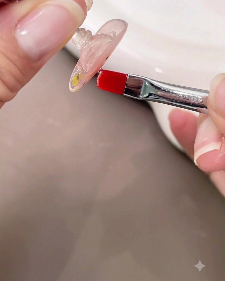 A hand holding a nail upside down while using a small brush to check the self-leveling clear builder gel apex.