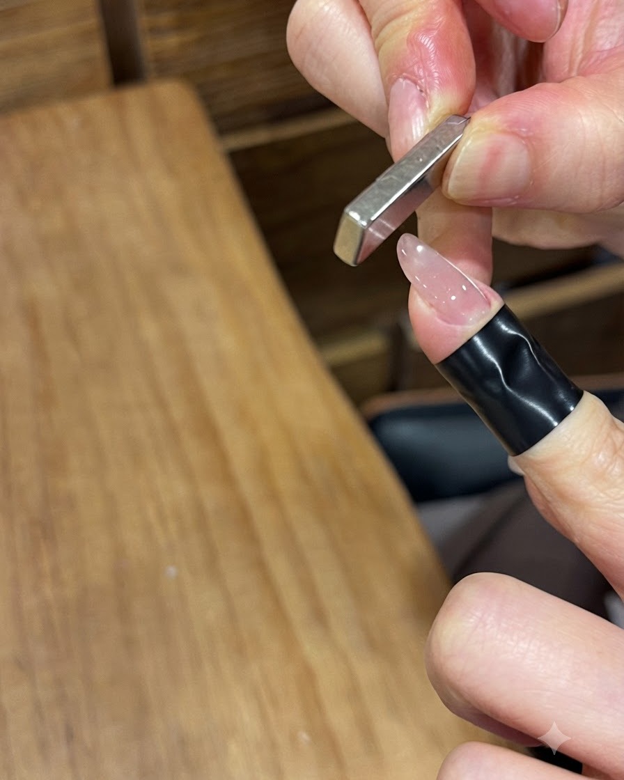 A rectangular metal bar magnet held vertically near a glossy gel-painted fingernail to push the magnetic particles.