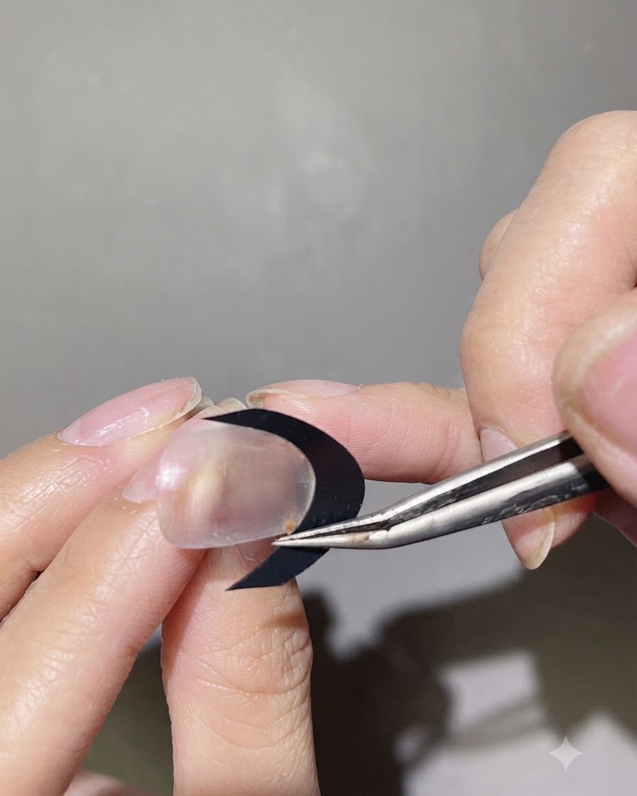 A pair of tweezers placing a black curved French sticker guide onto a clear nail surface.