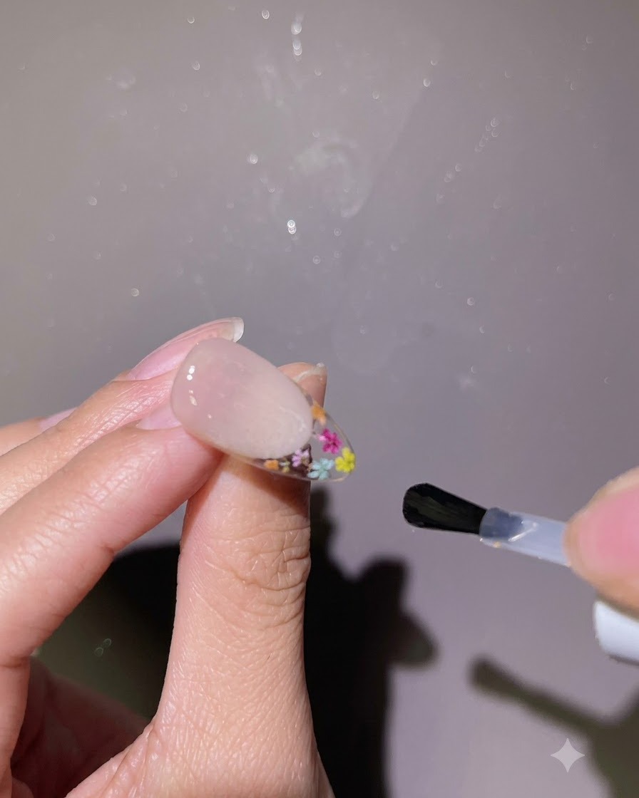 A brush applying a glossy top coat over the entire surface of a finished nail.