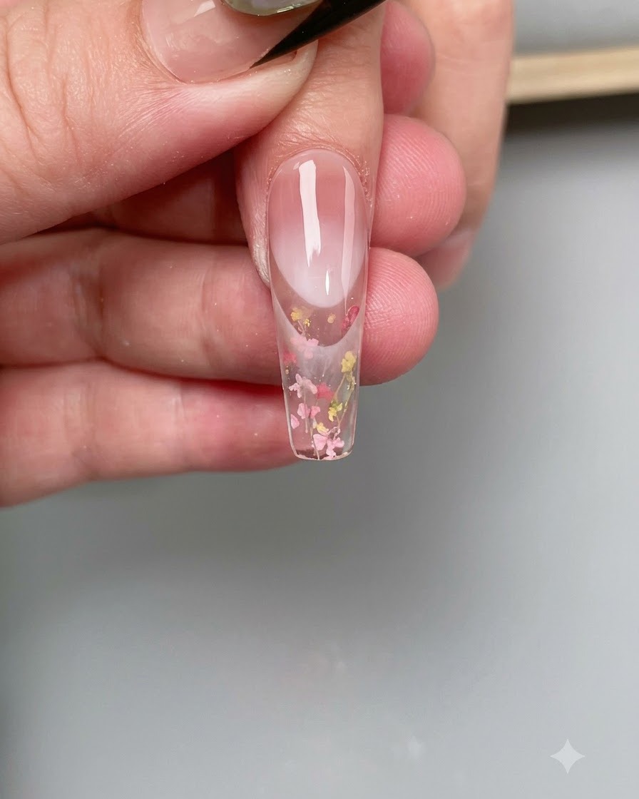 A fine brush applying clear base coat onto the surface of a clear nail tip.