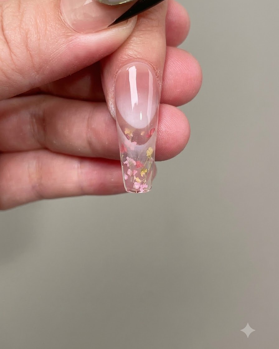 A pair of tweezers placing tiny pink and yellow dried flowers onto the wet nail gel.
