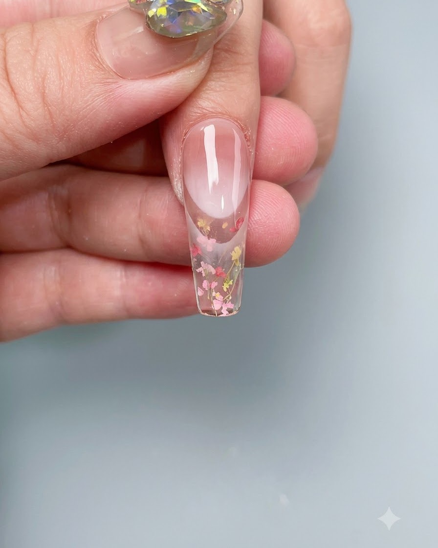 A nail with embedded dried flowers curing inside a professional UV/LED nail lamp.