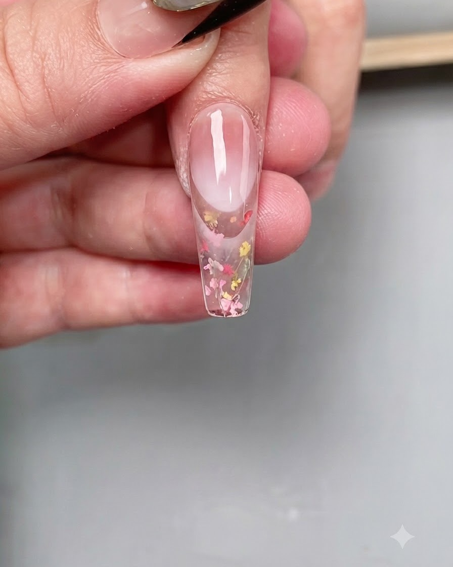 A fine nail art brush applying a clear diamond top coat precisely onto the tip of a long coffin-shaped nail.