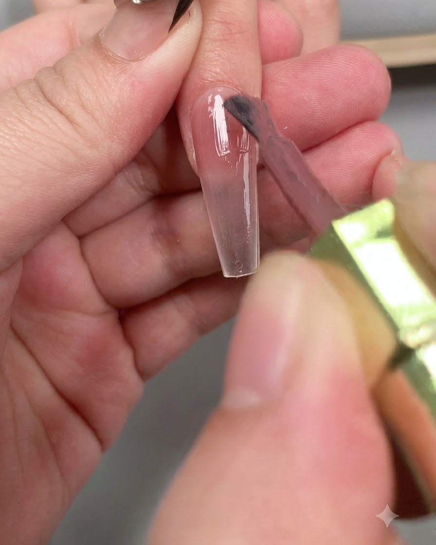 A brush applying a glossy layer of diamond top coat across the entire length of the nail.