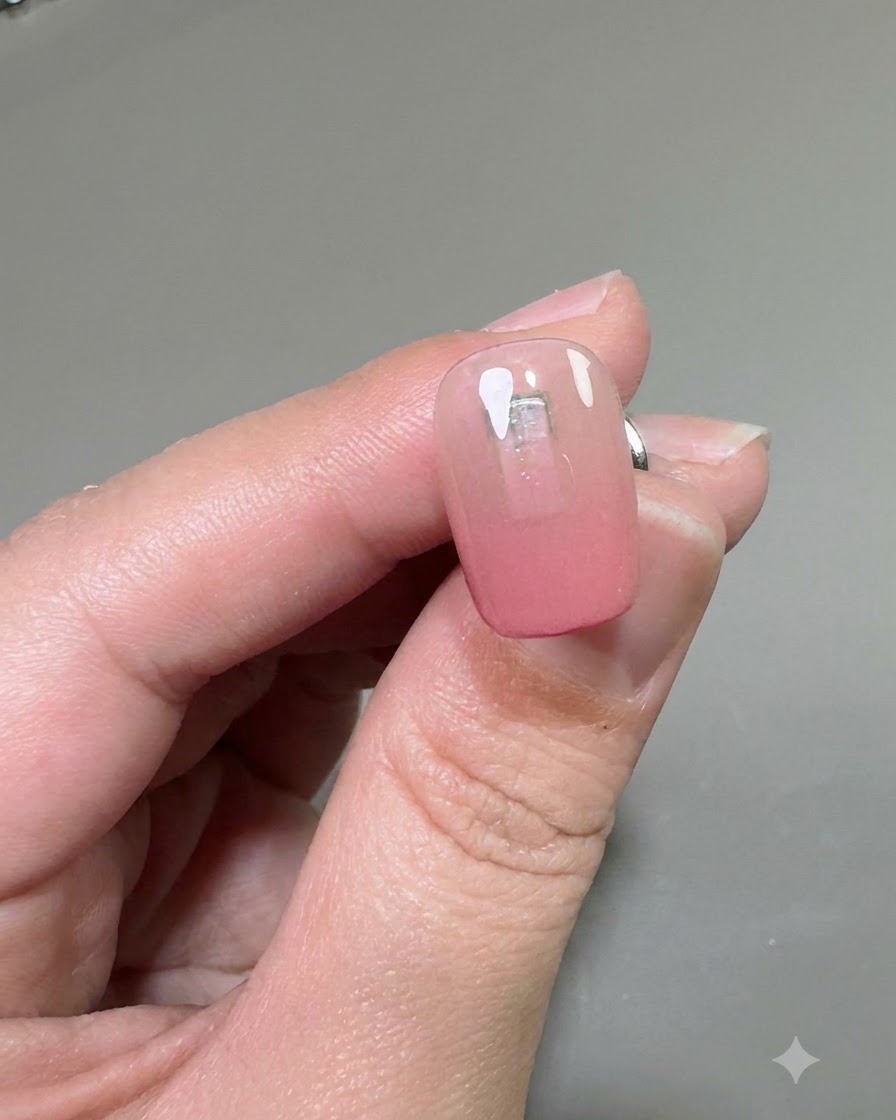 A close-up of a nail showing a clear coat of reinforcement gel applied over the pink gradient base.