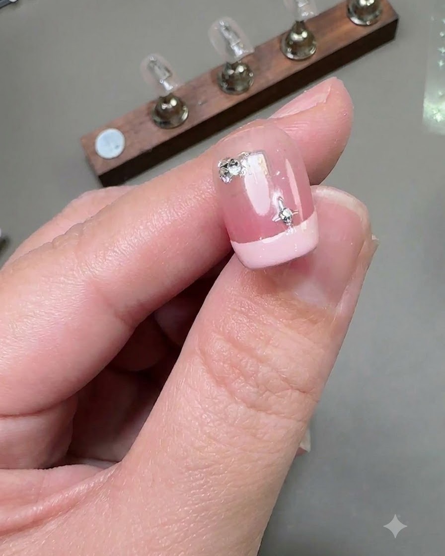 A close-up view of a short French manicure nail featuring a silver star sticker and a small round diamond affixed near the cuticle area.