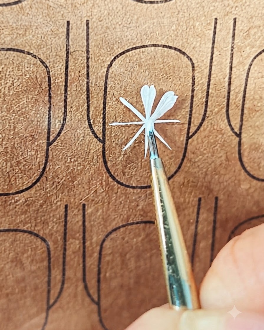 A fine nail art brush placing white gel to form a second petal on a practice board.